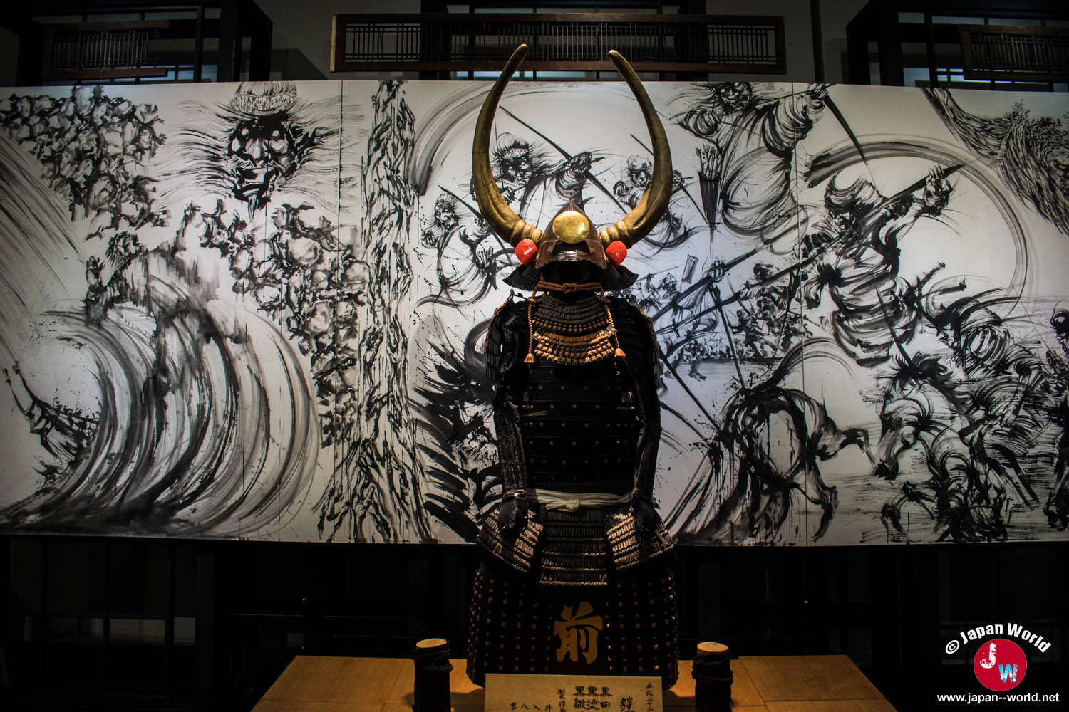 Armure de samouraï exposée devant une vaste peinture de bataille réalisée par Yuki Nishimoto