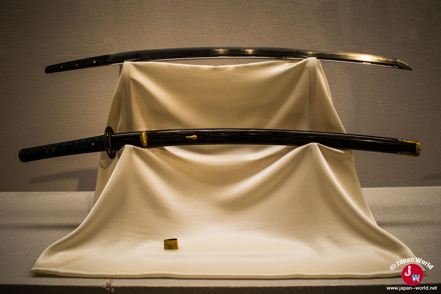 Lame de katana et fourreau noir exposés sur un drapé blanc