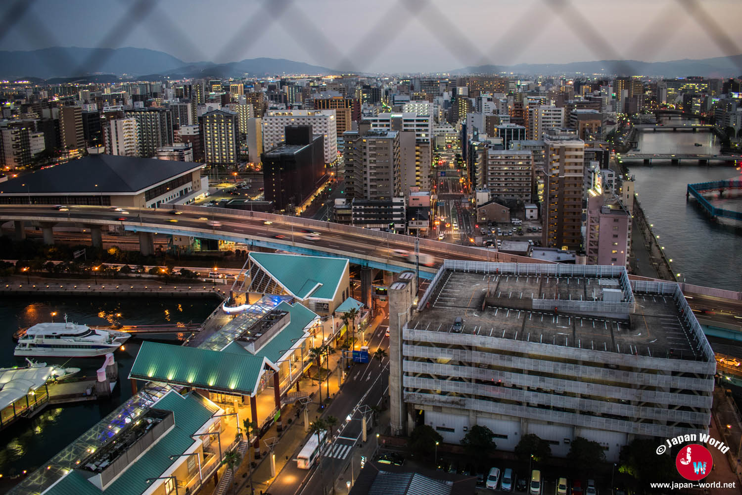 Ville de Fukuoka illuminée au crépuscule avec le port et la voie rapide au premier plan