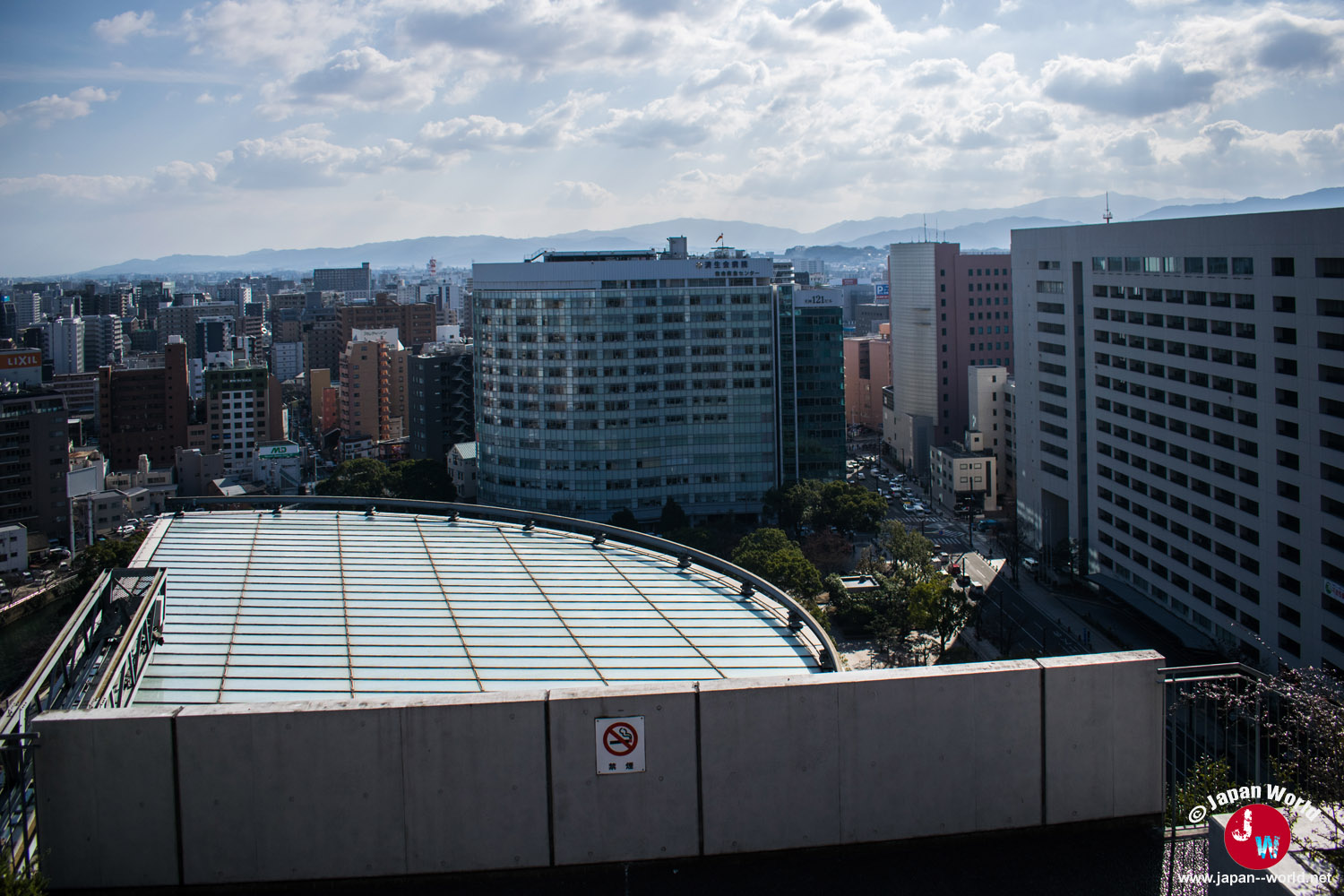 Toit incurvé d'ACROS Fukuoka devant les immeubles et les montagnes