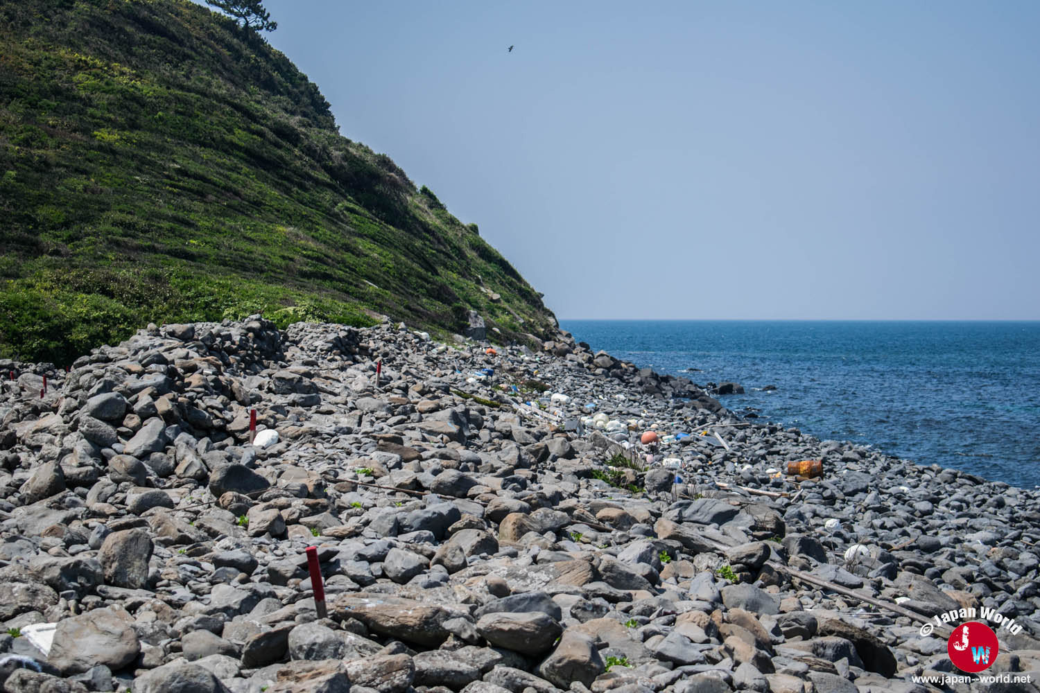 Plage de galets entre une colline et la mer à Ainoshima