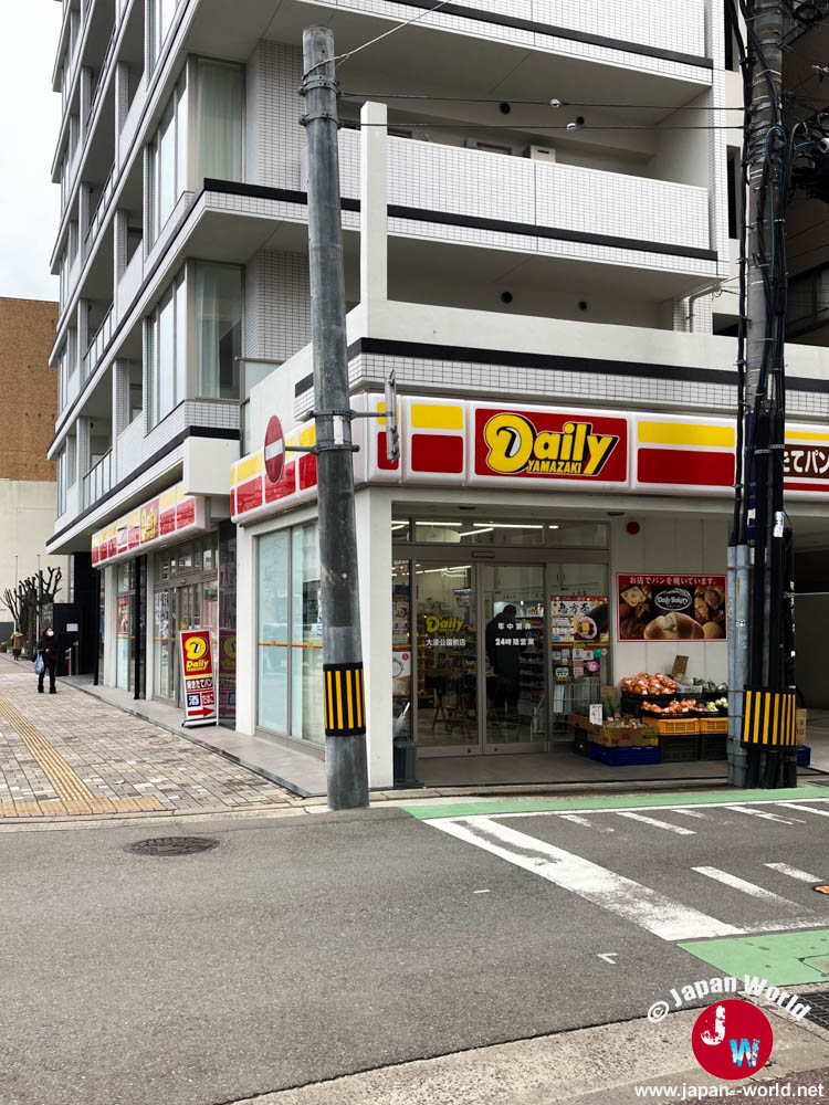 Magasin Daily Yamazaki en angle de rue avec des cagettes de fruits à l’entrée