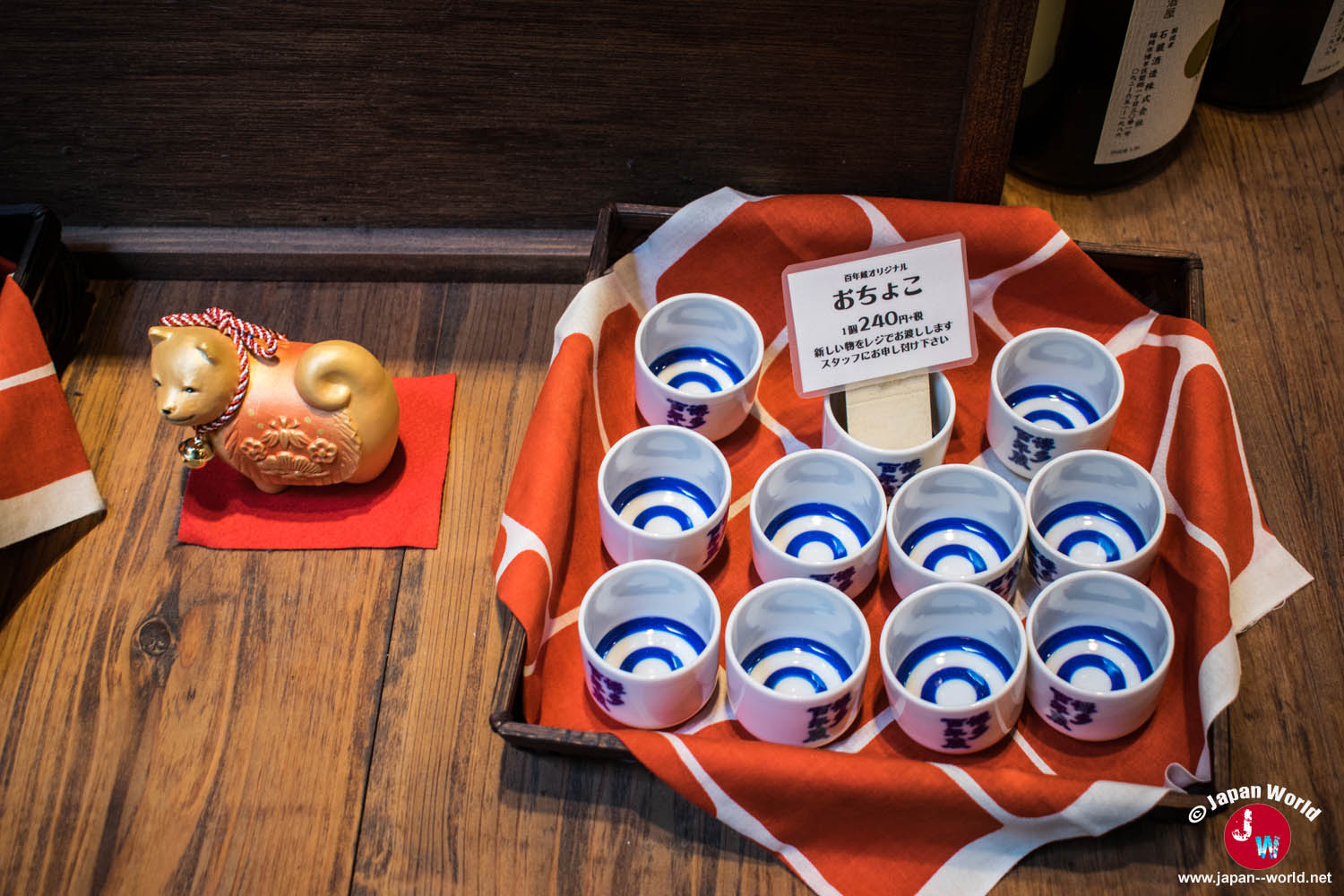 Petites coupes à saké blanches et bleues présentées à côté d'une figurine décorative