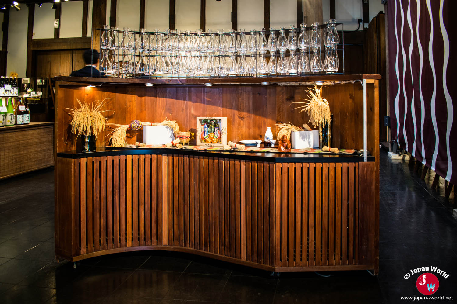 Présentoir en bois décoré de gerbes de riz et surmonté de bouteilles en verre dans la boutique Ishikura
