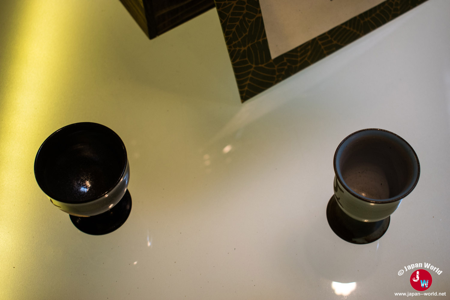 Deux coupes à saké sur pied exposées sur une table éclairée dans la boutique Ishikura
